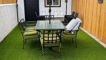 A patio with a glass table and chairs, a black and white striped umbrella, and a wooden fence.