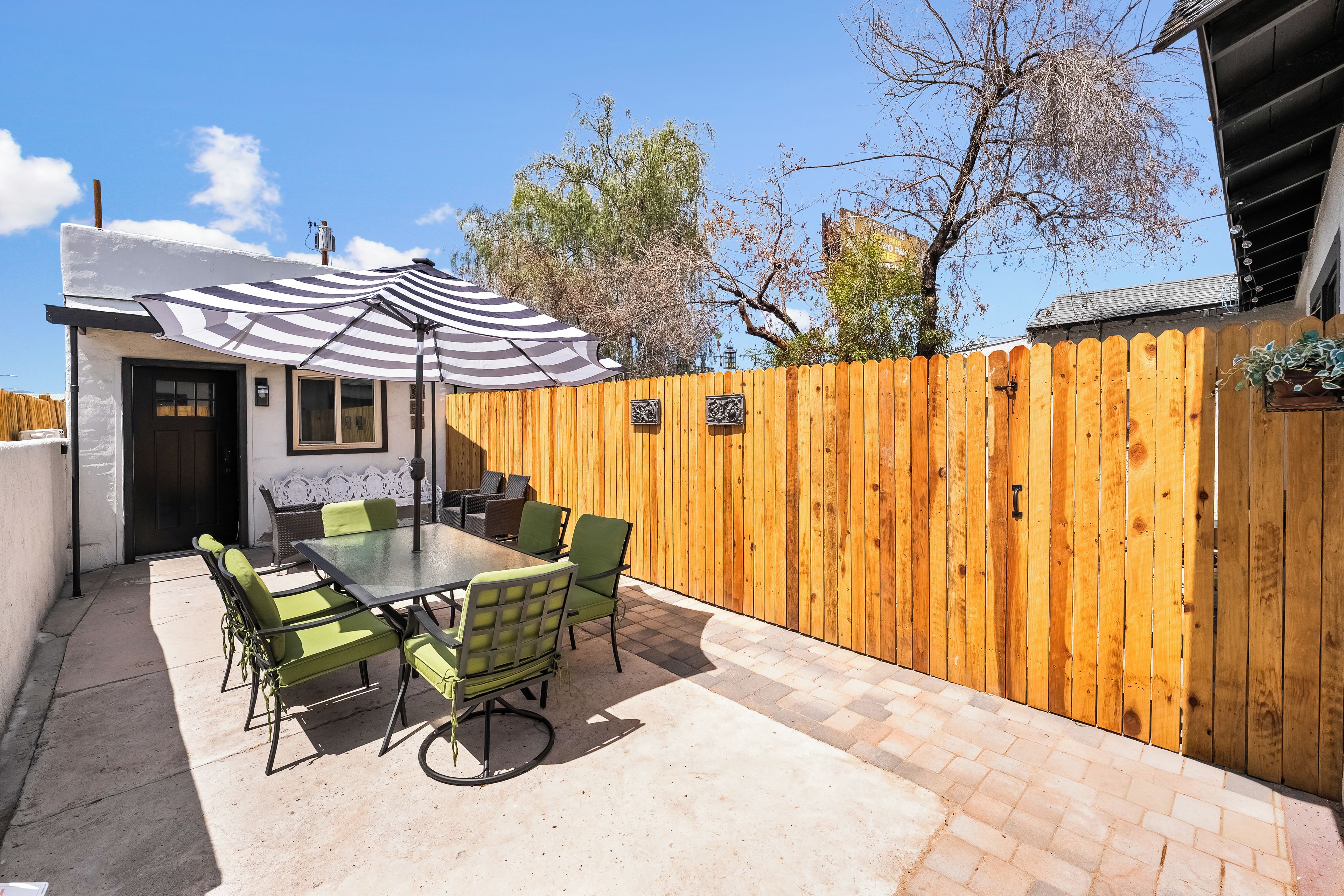 An outdoor patio with a table and chairs, a striped umbrella, and a wooden fence.