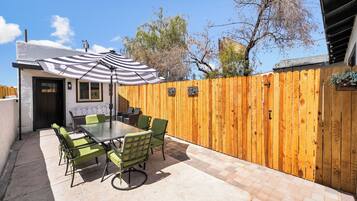 An outdoor patio with a table and chairs, a striped umbrella, and a wooden fence.