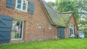 A brick building with a thatched roof, a stone foundation, and a small porch with white chairs. - A Historic Vacation at the Haubarg Tetenshof Kanada in Welt on the North Sea (Welt)