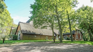 A traditional brick building with a thatched roof, surrounded by trees and a gravel driveway. - A Historic Vacation at the Haubarg Tetenshof Kanada in Welt on the North Sea (Welt)
