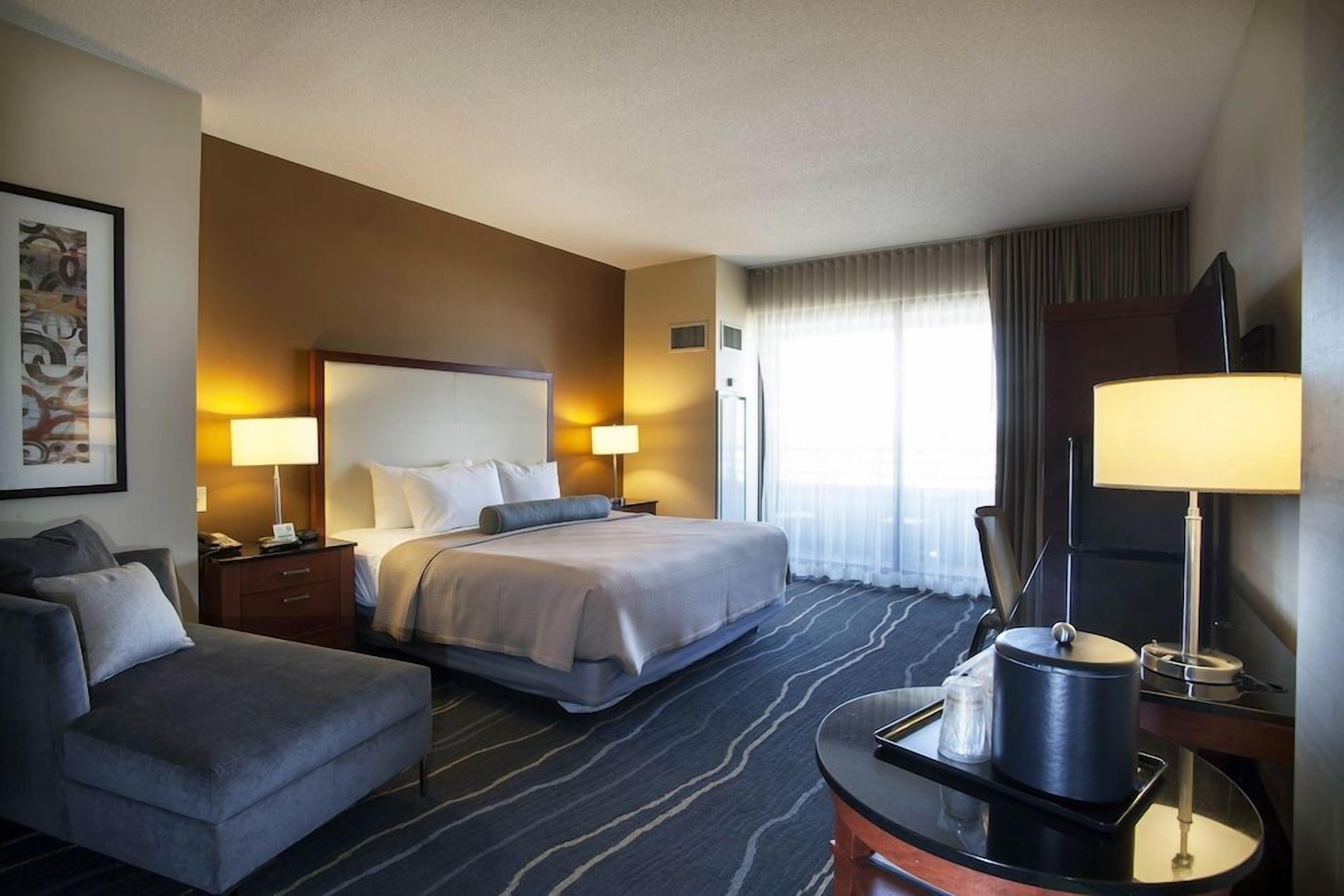 A hotel room with a bed, a sofa, a desk with a lamp, and a television.
