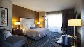 A hotel room with a bed, a sofa, a desk with a lamp, and a television.