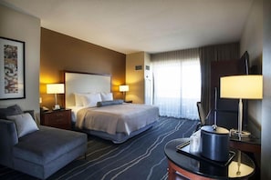 A hotel room with a bed, a sofa, a desk with a lamp, and a television.