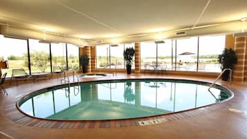 An indoor swimming pool with a tiled floor, surrounded by windows and chairs.
