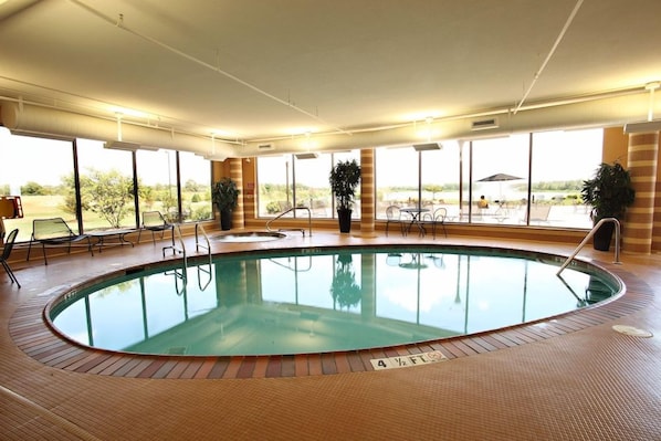 An indoor swimming pool with a tiled floor, surrounded by windows and chairs.