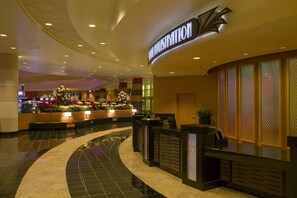 A hotel reception area with a curved reception desk, a floral arrangement, and a sign above the desk.