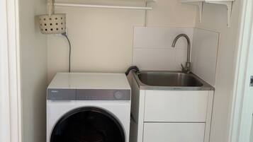 A compact laundry room with a front-loading washer, a sink, and storage shelves.