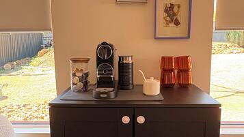Una kitchenette con cafetera, hervidor y un mueble pequeño. Encima de la encimera hay cuadros enmarcados en la pared.