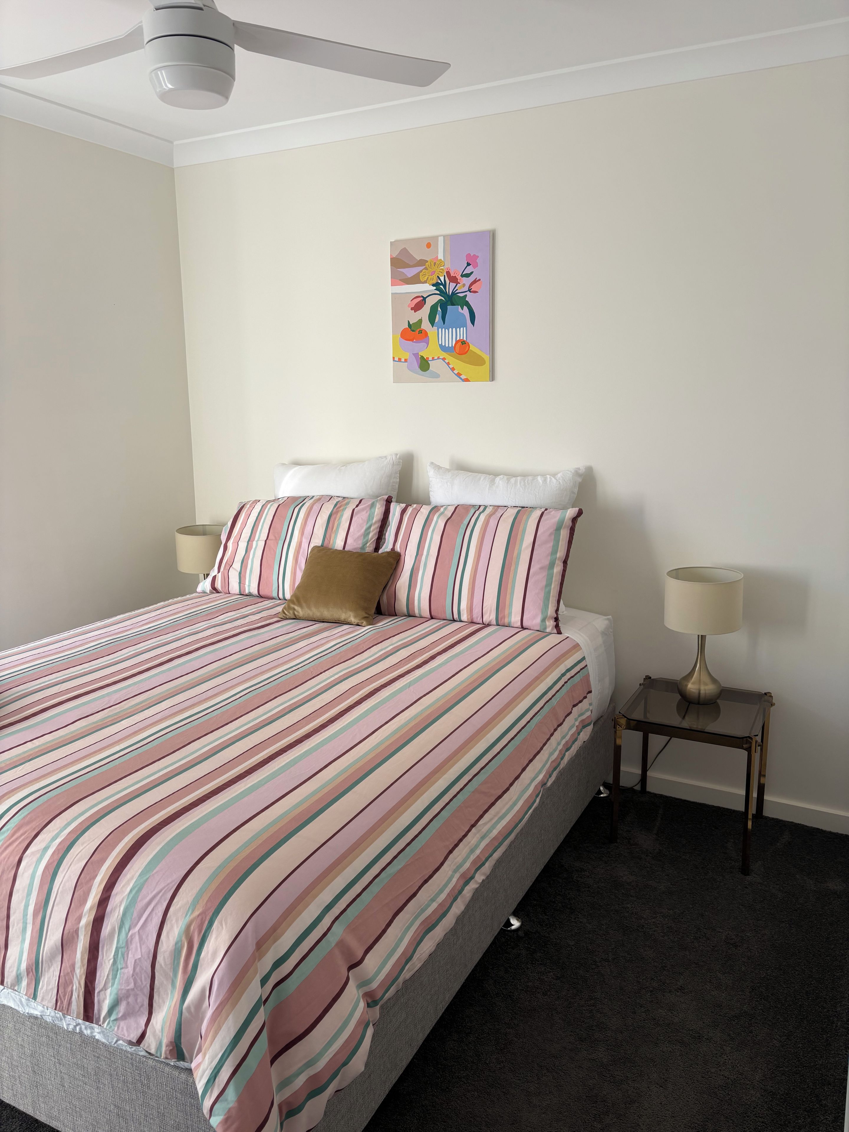 A neatly made bed with striped bedding, a single pillow, and a bedside table with a lamp.