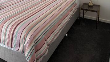 A neatly made bed with striped bedding, a single pillow, and a bedside table with a lamp.