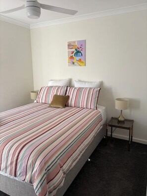 A neatly made bed with striped bedding, a single pillow, and a bedside table with a lamp.