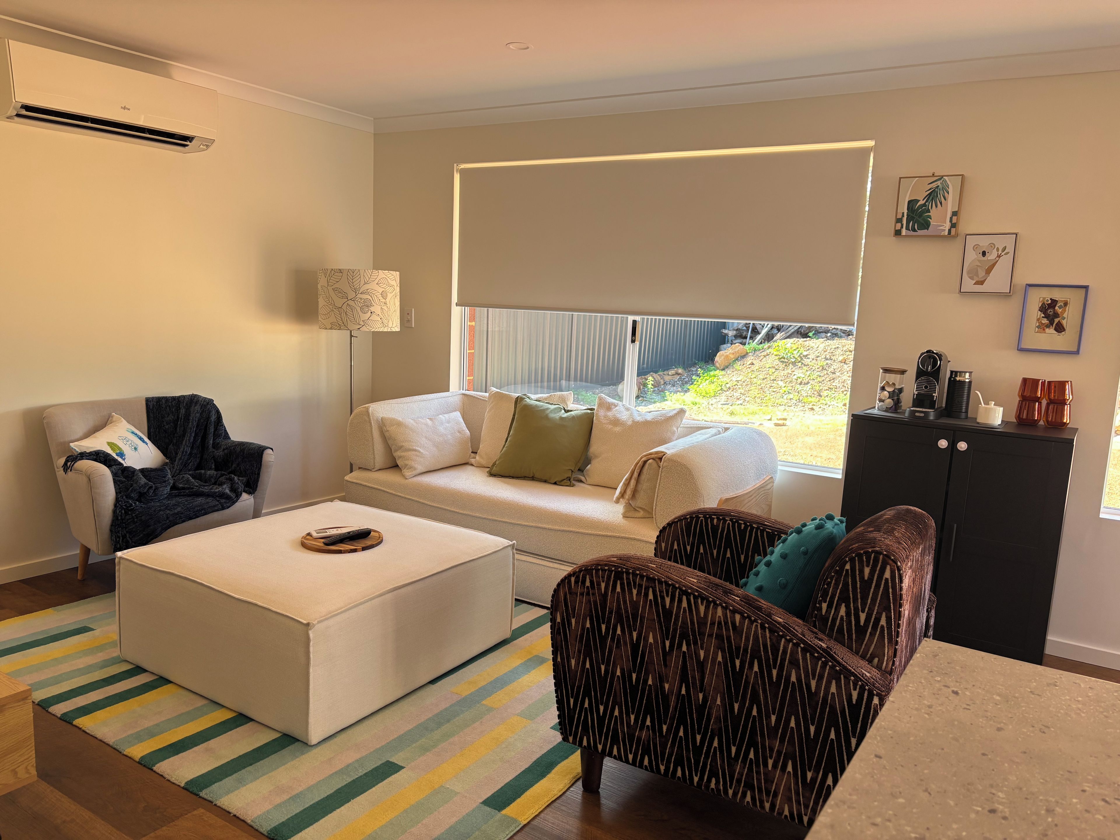 Una sala de estar con sofá, sillón, otomanas y una lámpara.