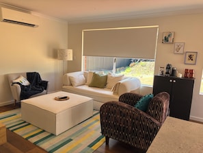 Una sala de estar con sofá, sillón, otomanas y una lámpara.