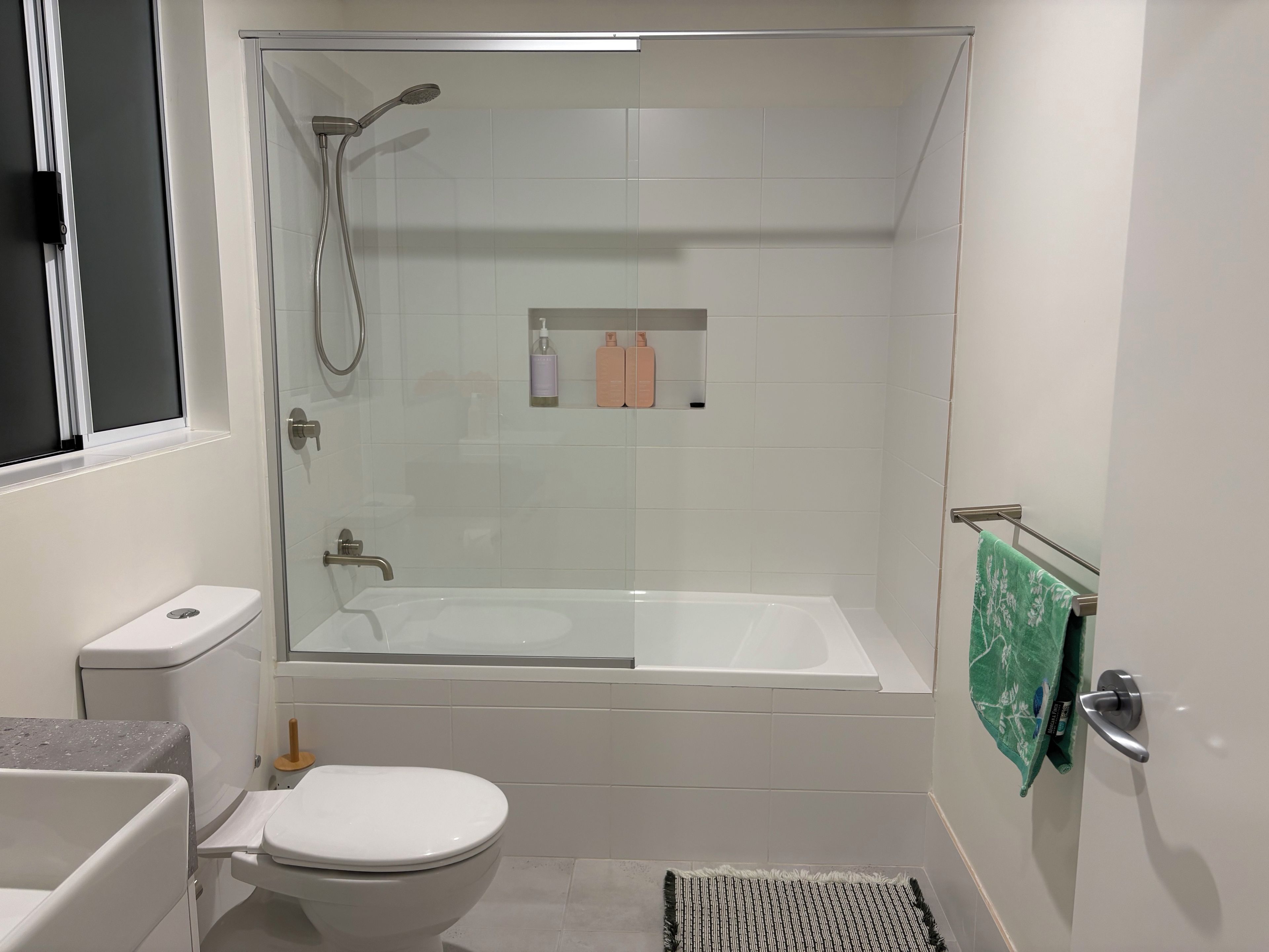 A bathroom with a glass-enclosed shower, a white bathtub, a toilet, and a towel rack with a green towel.