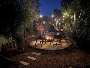 An outdoor patio area with a fire pit, wooden chairs, and string lights. - Grove Road Retreat - walk to Lesmurdie Falls! (Lesmurdie)