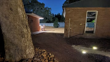 Uma estrada de terra batida leva a um edifício de tijolos com um deck de madeira e uma árvore.