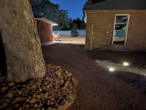 A dirt driveway leading to a brick building with a wooden deck and a tree. - Grove Road Retreat - walk to Lesmurdie Falls! (Lesmurdie)
