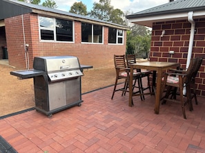 Un patio con una parrilla, una mesa de madera y sillas.