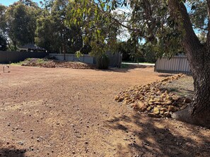 A gravel area with trees and a fenced structure.