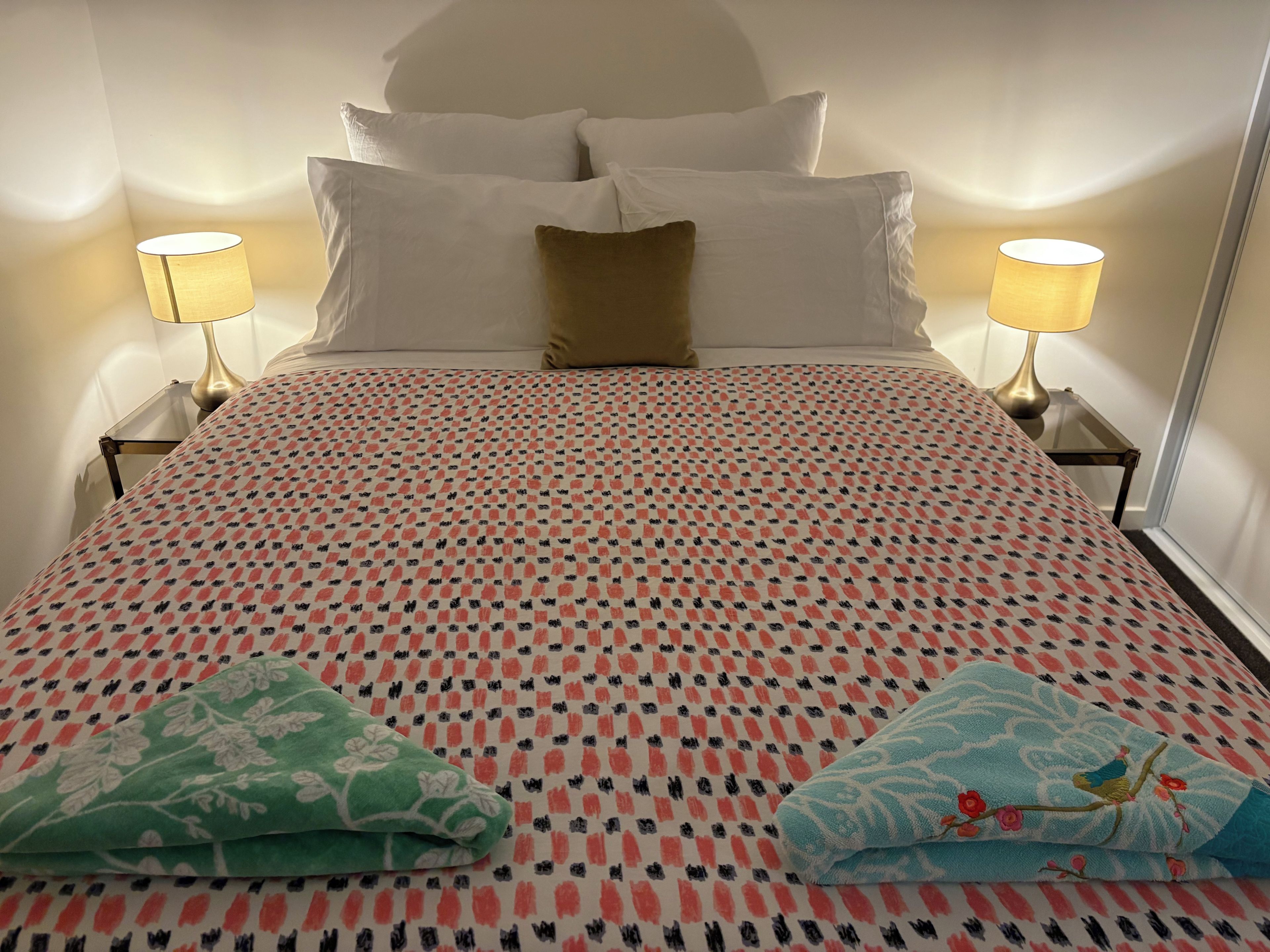 Un llit ben fet amb un edredó estampat, dos coixins, dues làmpades de nit i dues mantes doblegades.