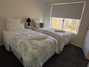 A bedroom with two beds, a nightstand, a lamp, and a window with a view. - Grove Road Retreat - walk to Lesmurdie Falls! (Lesmurdie)