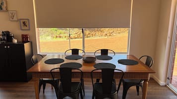 Un comedor con una mesa y sillas de madera, un ventanal con vista a un paisaje rocoso y una kitchenette con cafetera.