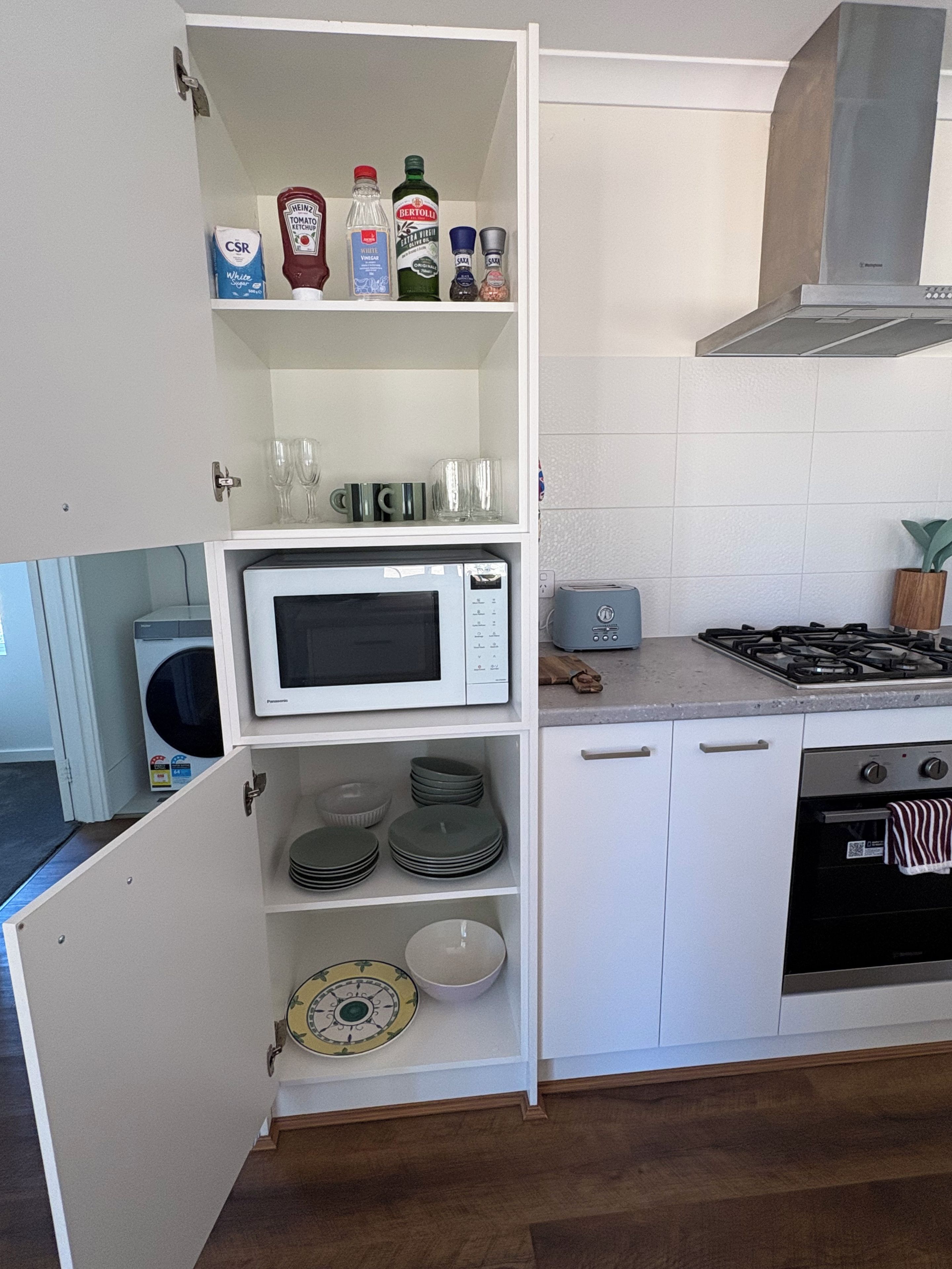 Una cocina con microondas, tostadora, estufa y estantes con utensilios de cocina.