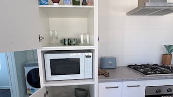 Una cocina con microondas, tostadora, estufa y estantes con utensilios de cocina.