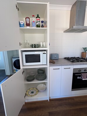 A kitchen with a microwave, toaster, stove, and shelves with kitchen items. - Grove Road Retreat - walk to Lesmurdie Falls! (Lesmurdie)