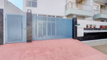Una entrada protegida por un portón de metal y un piso de tejas rojas que conduce a un edificio con balcón.