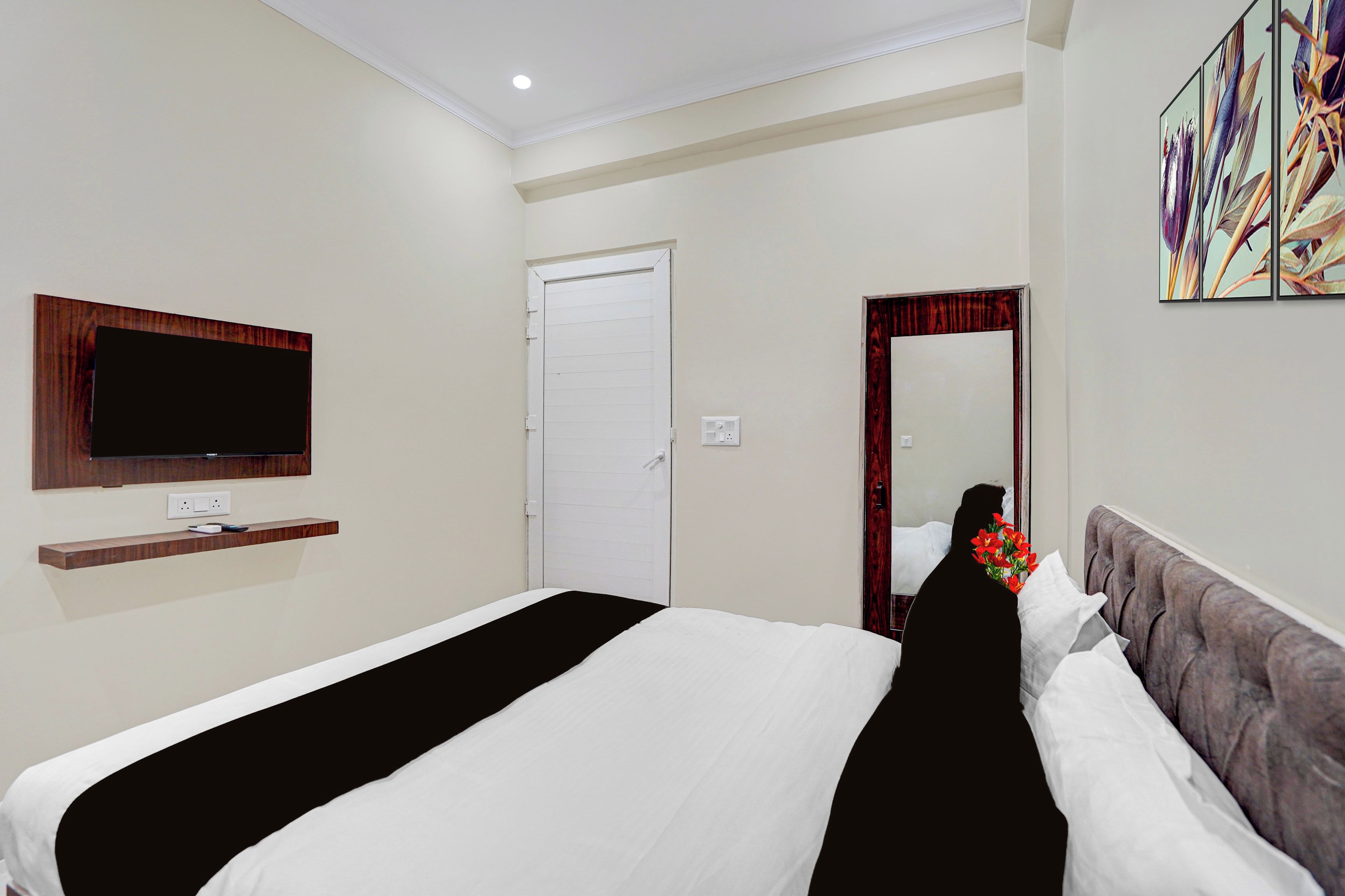 A hotel room with a bed, a television mounted on the wall, a door, and a mirror.
