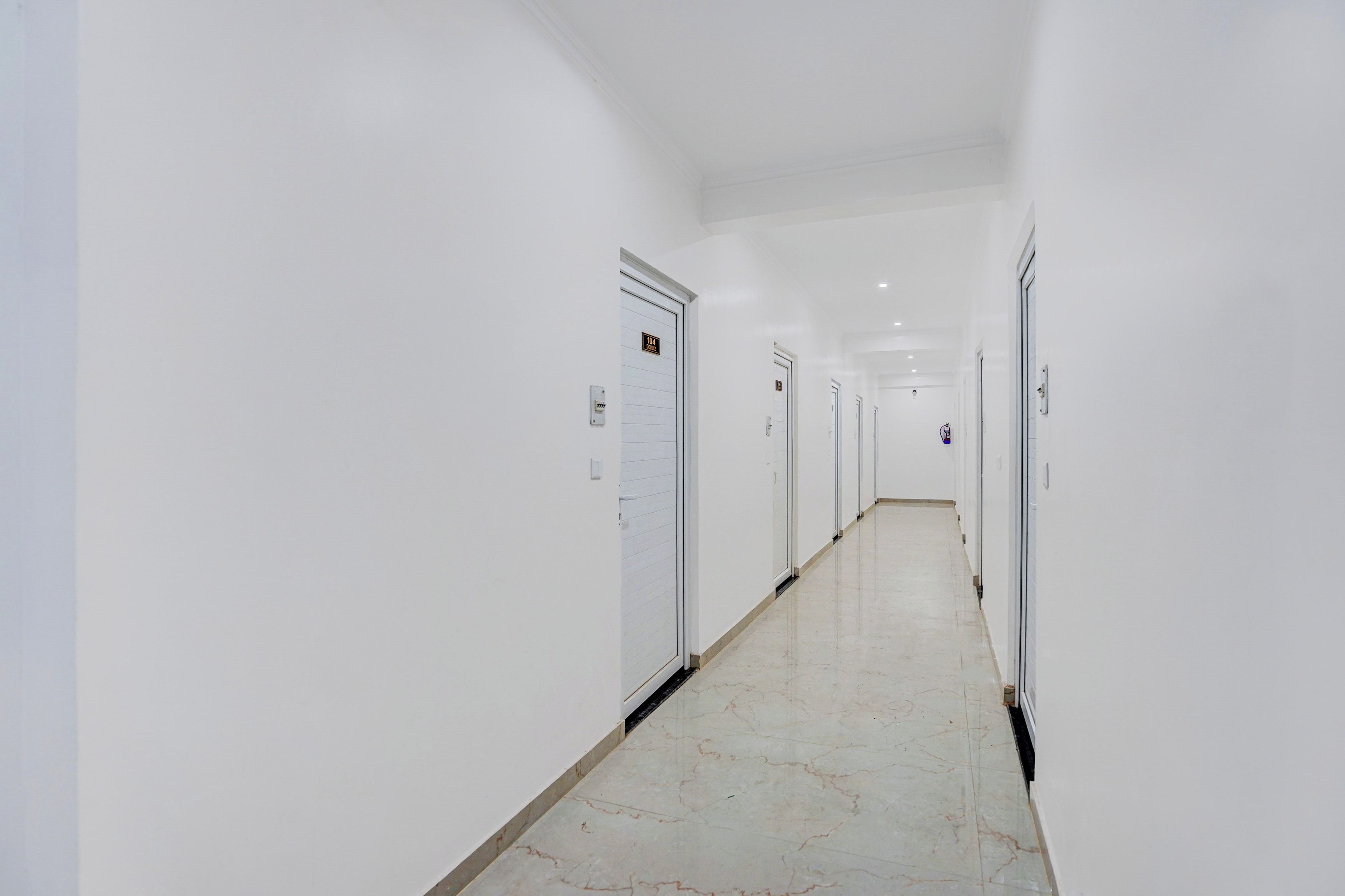 A long, narrow hallway with white walls and doors, leading to a series of rooms.