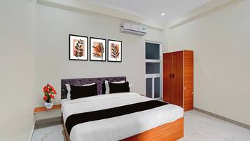 Un dormitorio con cama, mesita de noche con un florero, armario y tres cuadros en la pared.