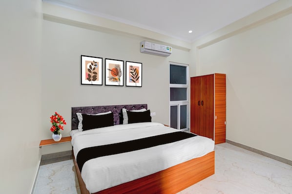 A bedroom with a bed, a nightstand with a vase of flowers, a wardrobe, and three framed artworks on the wall. - Townhouse Lucknow Formerly Pine Villa (Lucknow)