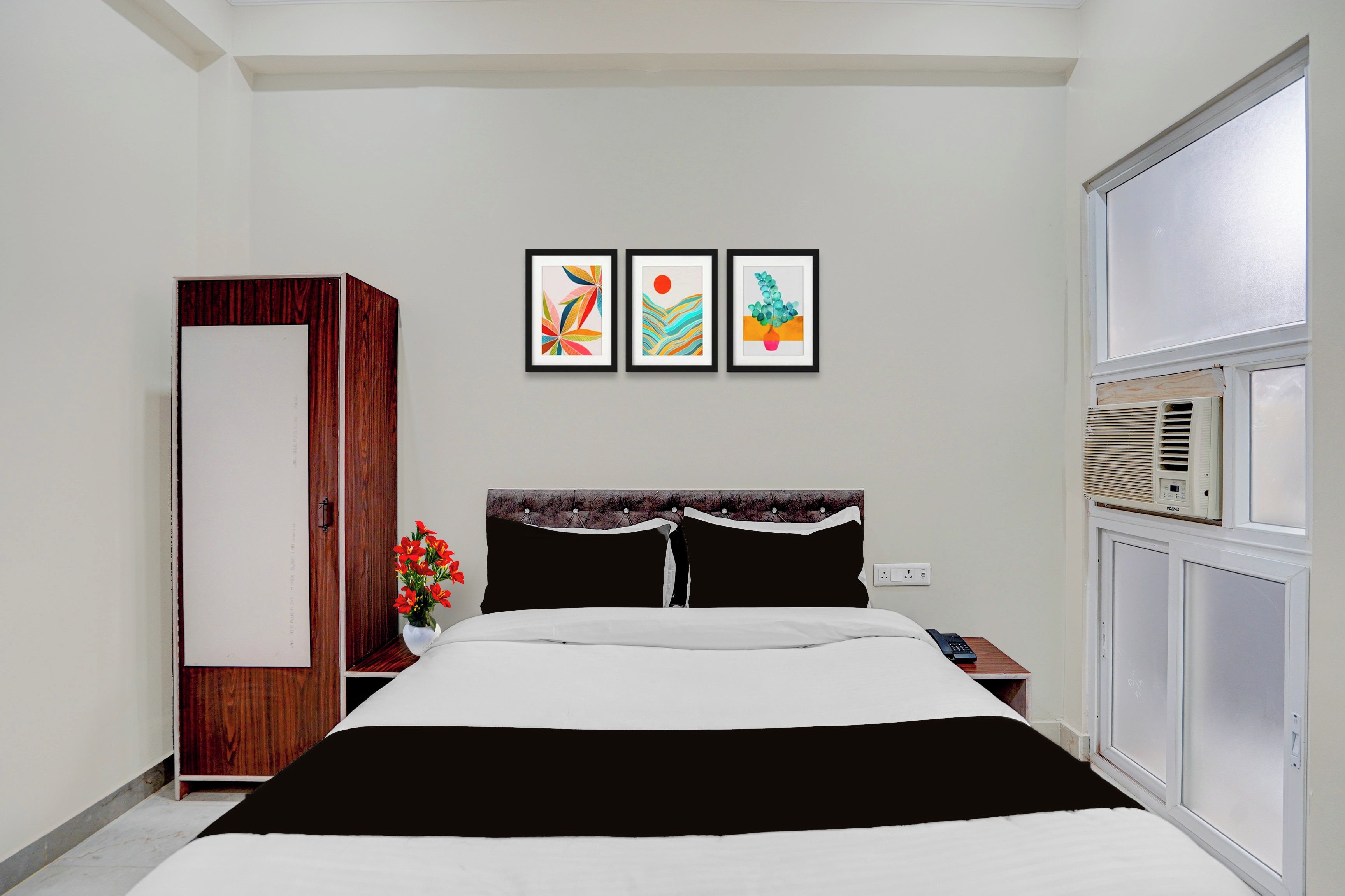 Un dormitorio con cama, armario, mesita de noche, calentador de pared y tres obras de arte enmarcadas.