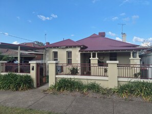 A two-story house with a red roof, a gated driveway, and a number 92 sign on the gate.