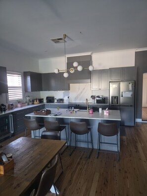 Eine moderne Küche mit einer zentralen Kochinsel, Barhocker, einem Holzes Esstisch und einem Edelstahl-Kühlschrank.
