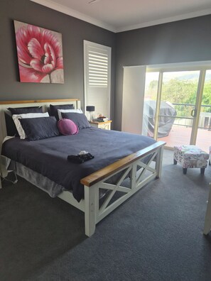 Ein Schlafzimmer mit Bett, Nachttisch, Lampe, einem Fenster mit Jalousien und einem Balkon mit Tisch.