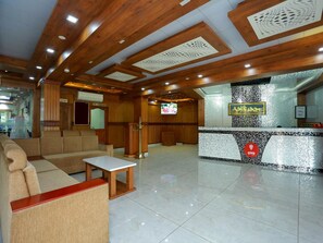 Un vestíbulo de hotel con mostrador de recepción, zona de estar y una pantalla de televisión.
