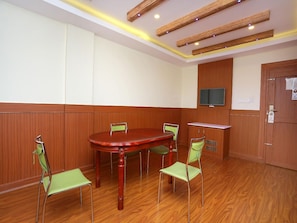 A conference room with a wooden table and four chairs, a television mounted on the wall, and a door with a sign. - Capital O 14702 Kovilakam Residency (Thrissur)