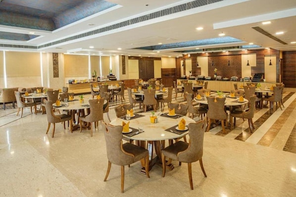 A spacious hotel dining area with multiple round tables and chairs, a central bar, and a high ceiling with skylights. - Opulent by Ferns N Petals Chattarpur (New Delhi)