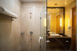 Un bany modern amb dutxa tancada amb vidre, paret amb mosaics de marbre i un lavabo amb mirall.