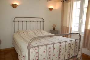 Une chambre à coucher avec un lit en métal, une table de chevet avec une lampe et une fenêtre avec des rideaux.