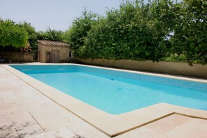 Une piscine rectangulaire dont le bord est recouvert de carreaux, entourée d’un mur de pierre et d’une végétation luxuriante.