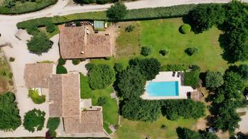 An aerial view of a property with a swimming pool, multiple buildings with flat roofs, and surrounding greenery.
