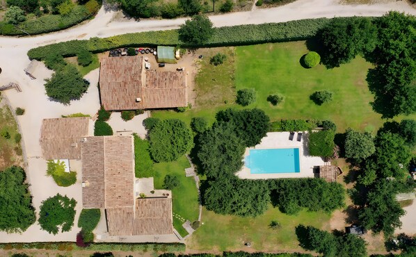 Vue aérienne d’une propriété dotée d’une piscine, de plusieurs bâtiments aux toits plats et d’un espace vert environnant.