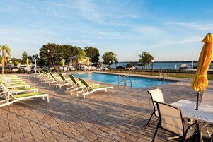 Un área junto a la piscina con sillones de descanso y sombrillas, una piscina y vistas al agua.