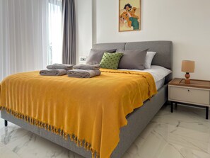 A neatly made bed with a yellow blanket, grey pillows, and a small bedside table with a lamp. - Qoople Elize B20 - Cozy 1-bedroom apartment in Alanya (Alanya)
