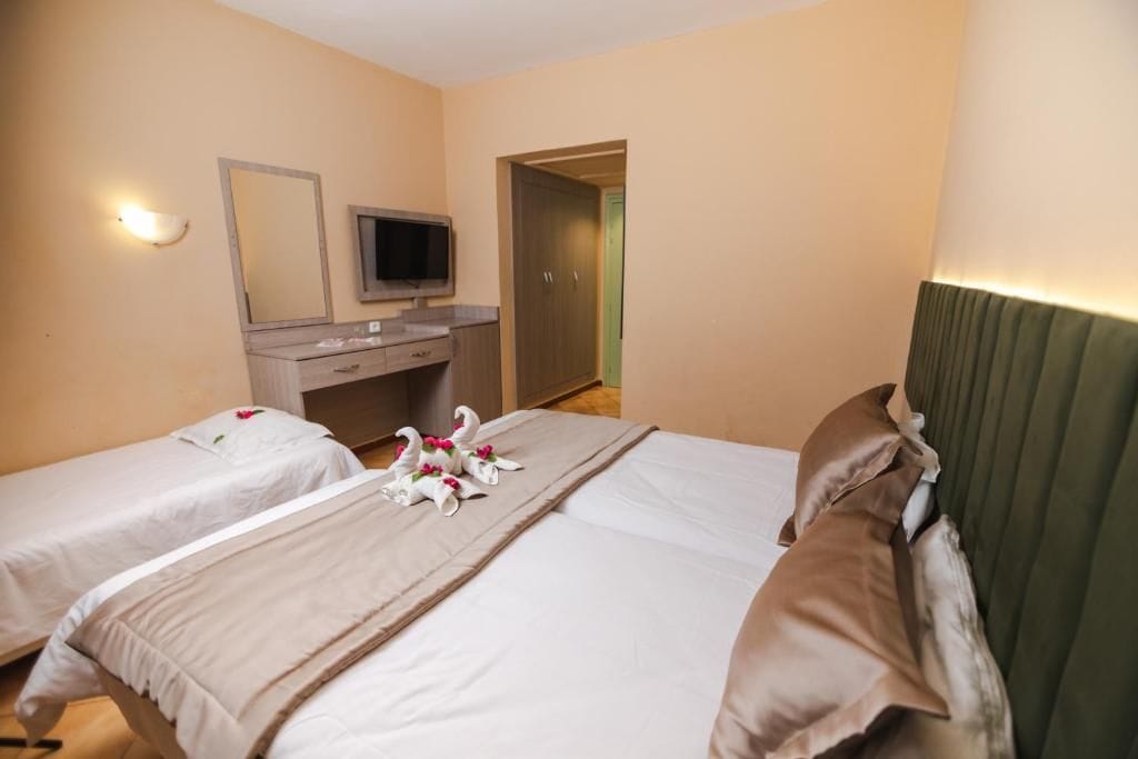 Habitación de hotel con dos camas, un escritorio con televisor y un espejo.